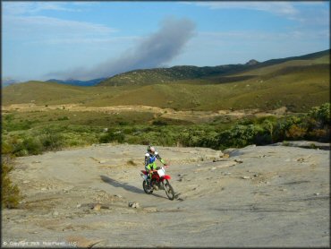 Woman on Honda dirt bike riding up section of solid rock.