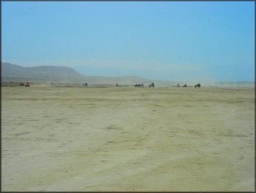 Group of ATVs, dirt bikes and dune buggies riding on lake bed.