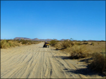 Man on Honda 250 ATV turning around on wide and sandy wash.