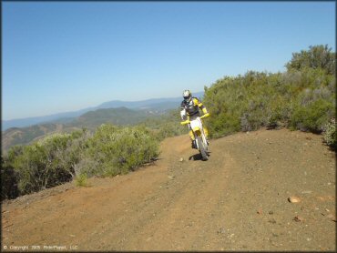 Man on Suzuki RM-250 dirt bike traveling down hard packed 4x4 trail.