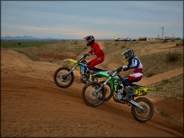 A Kawasaki KX450 and a Suzuki RM450 Battling Over Round Top Jump Face