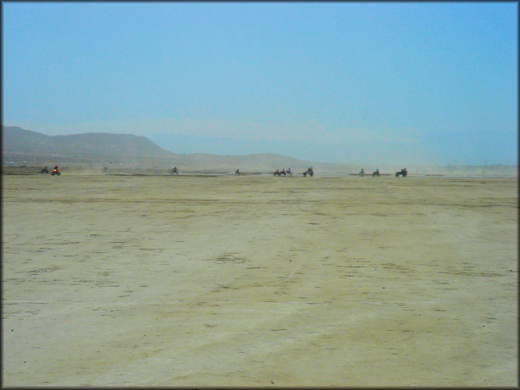 Group of ATVs, dirt bikes and dune buggies riding on lake bed.