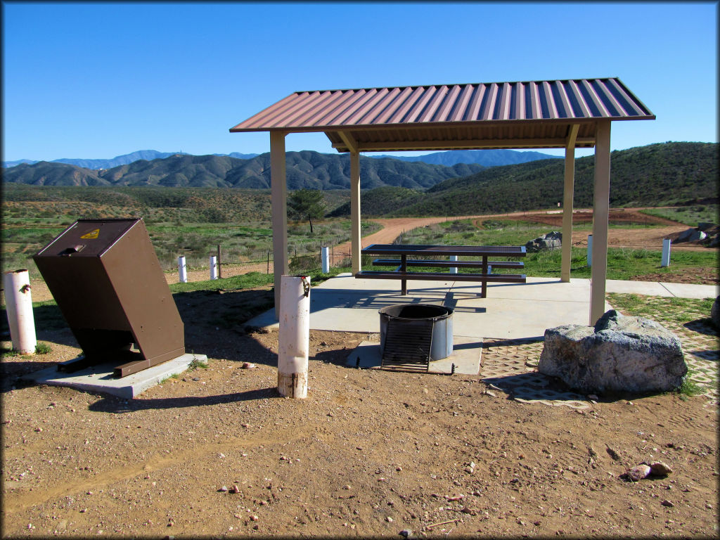 Photo of shade gazebo on concrete pad with picnic table, fire ring and trash receptacle.