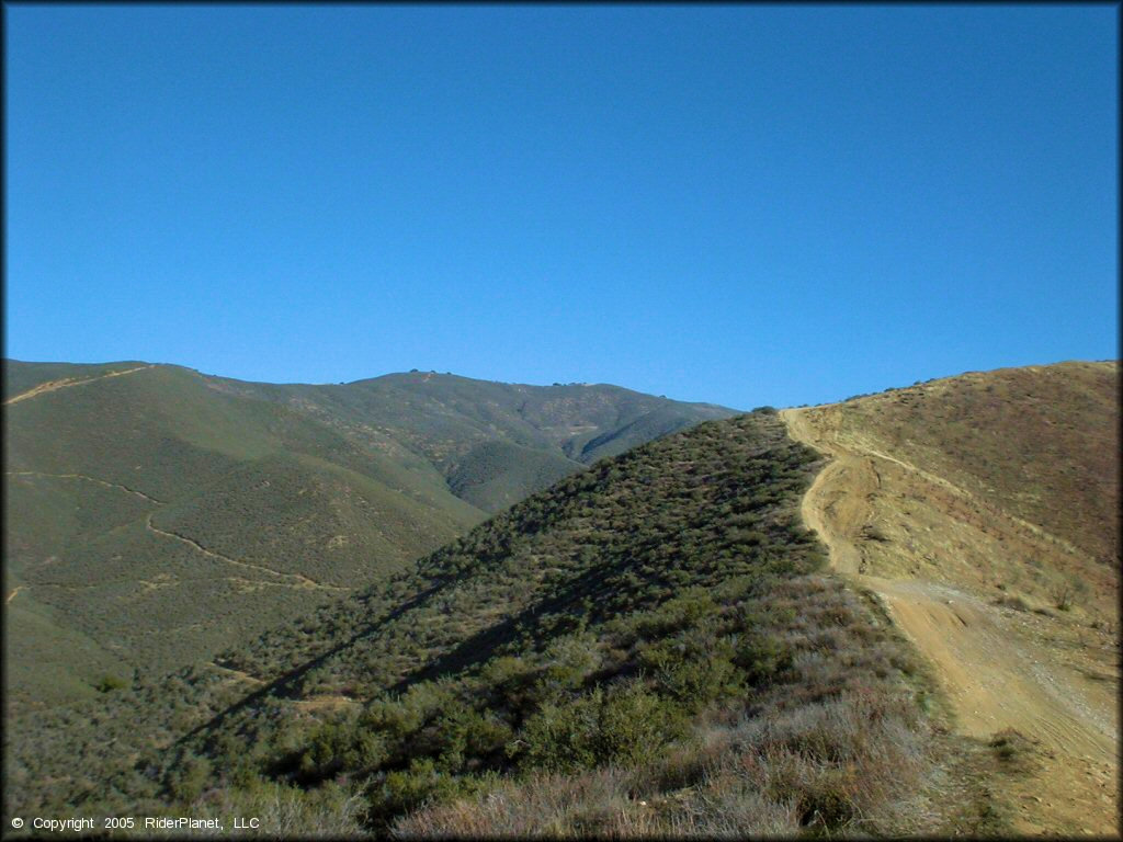 A close up photo of narrow trail following ridgeline of steep hill.